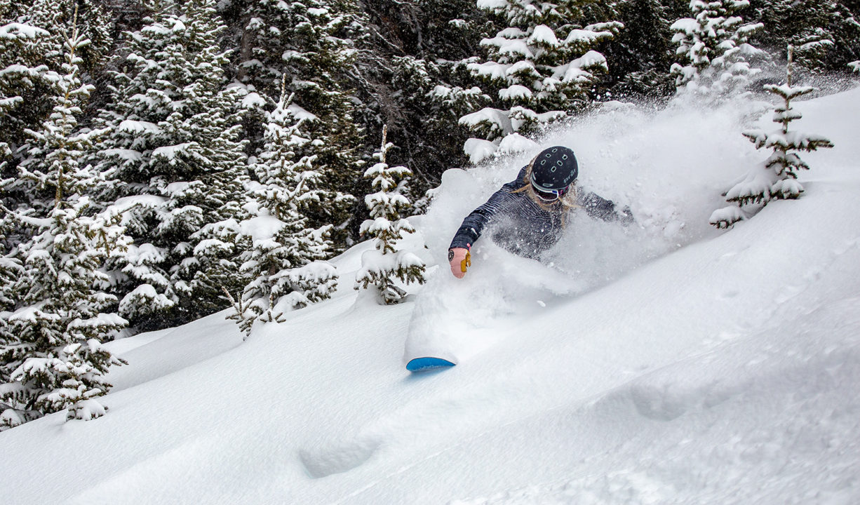 A female snowboarder rides through fresh powder at Copper Mountain.