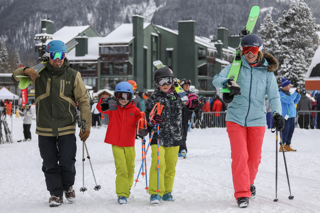 A family of four walks on the snow at Copper Mountain with ski gear in hand.